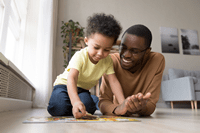 A young child and an adult are lying on the floor together, working on a puzzle. The adult smiles warmly, watching the child place a piece. They appear to be in a cozy living room, enjoying moments similar to those fostered by ABA near Chester County PA.
