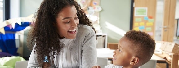 A woman and a young child are sitting together in a classroom, smiling at each other—reflecting the positive connection fostered by ABA therapy near Philadelphia PA.
