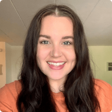 Smiling woman with long, dark hair wearing an orange top, indoors with light-colored walls and a ceiling visible—perfect for representing ABA near Chester County PA.