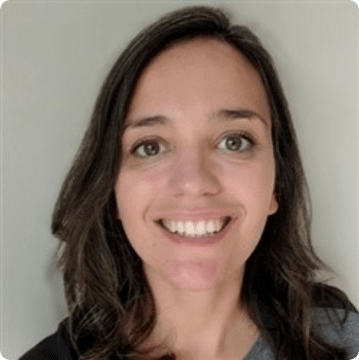 A woman with shoulder-length brown hair and green eyes smiles at the camera against a plain light-colored background, representing caring professionals providing ABA therapy near Philadelphia PA.
