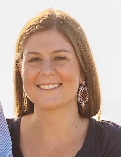 A woman with straight, light brown hair smiles at the camera. She is wearing a dark top and large, sparkling earrings. The bright, softly blurred background evokes the welcoming atmosphere of autism therapy near Chester County PA.