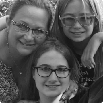 A black and white photo of three people, all wearing glasses, smiling closely together. The adult has her arm around the two children—all with long hair—celebrating family moments and autism services near Montgomery County PA.