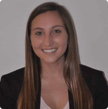 A young woman with straight brown hair, wearing a black blazer over a light-colored top, smiles at the camera against a plain light background, representing autism treatment near Delaware County PA.
